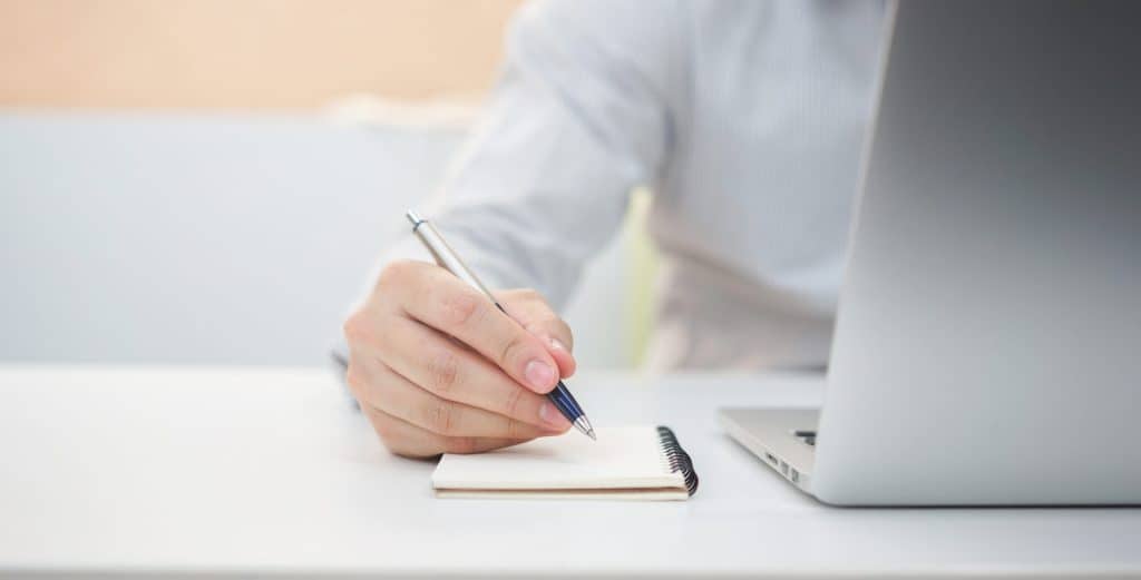 An employee uses paper, pen and a computer to figure out IT Cost for their business.